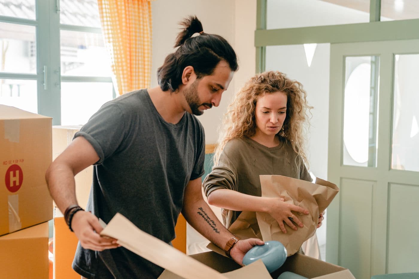 Two people wrapping kitchenware in paper before placing it in a moving box